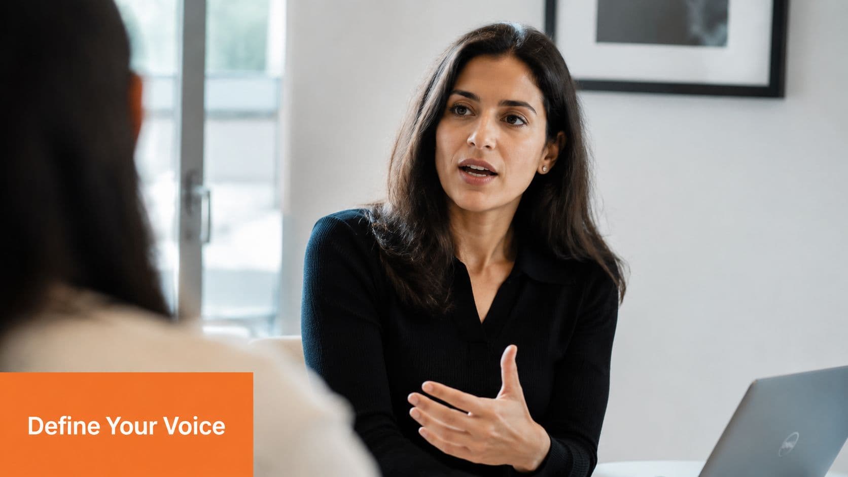 A woman in a black shirt speaks to a colleague during a professional office meeting.